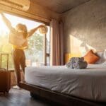 Mujer disfrutando con los brazos abiertos mientras mira el amanecer por la ventana del hostal hotel en Barcelona España