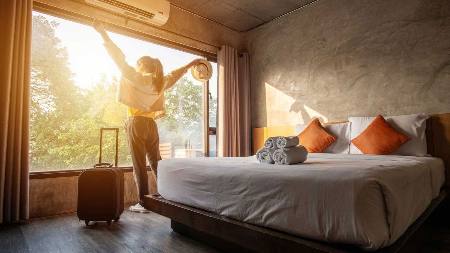 Mujer disfrutando con los brazos abiertos mientras mira el amanecer por la ventana del hostal hotel en Barcelona España