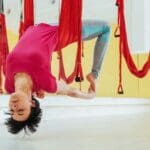 Mujer vestida de rojo colgando de arnés en una clase de aeroyoga en España