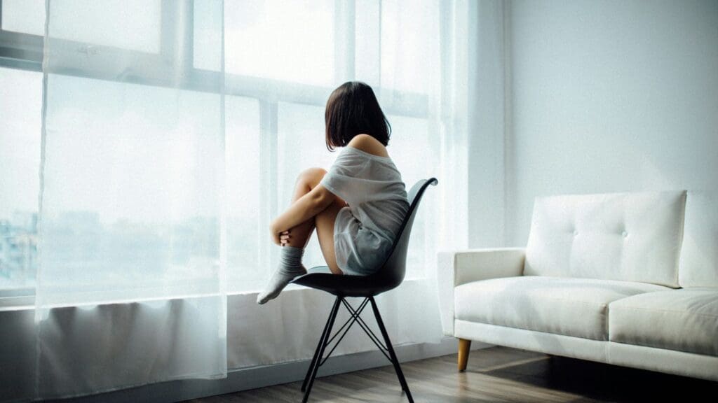 Adolescente sentada sobre una silla frente a la ventana de una habitación. psicoterapia para adolescentes en España