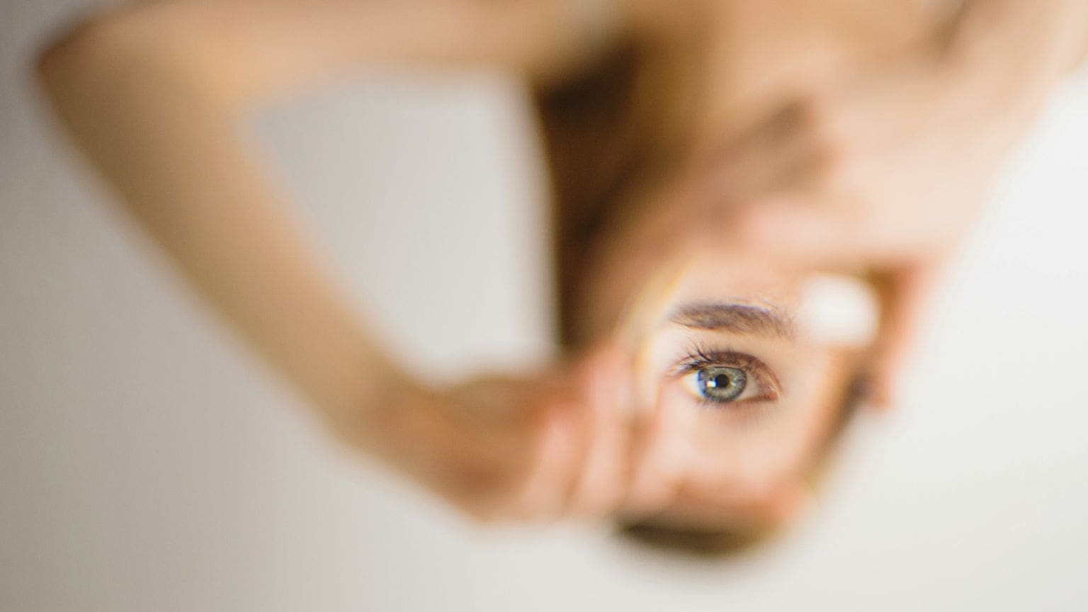 Imagen borrosa de mujer invertida haciendo señal con sus manos y dentro de ellas se ve un ojo de mujer observando