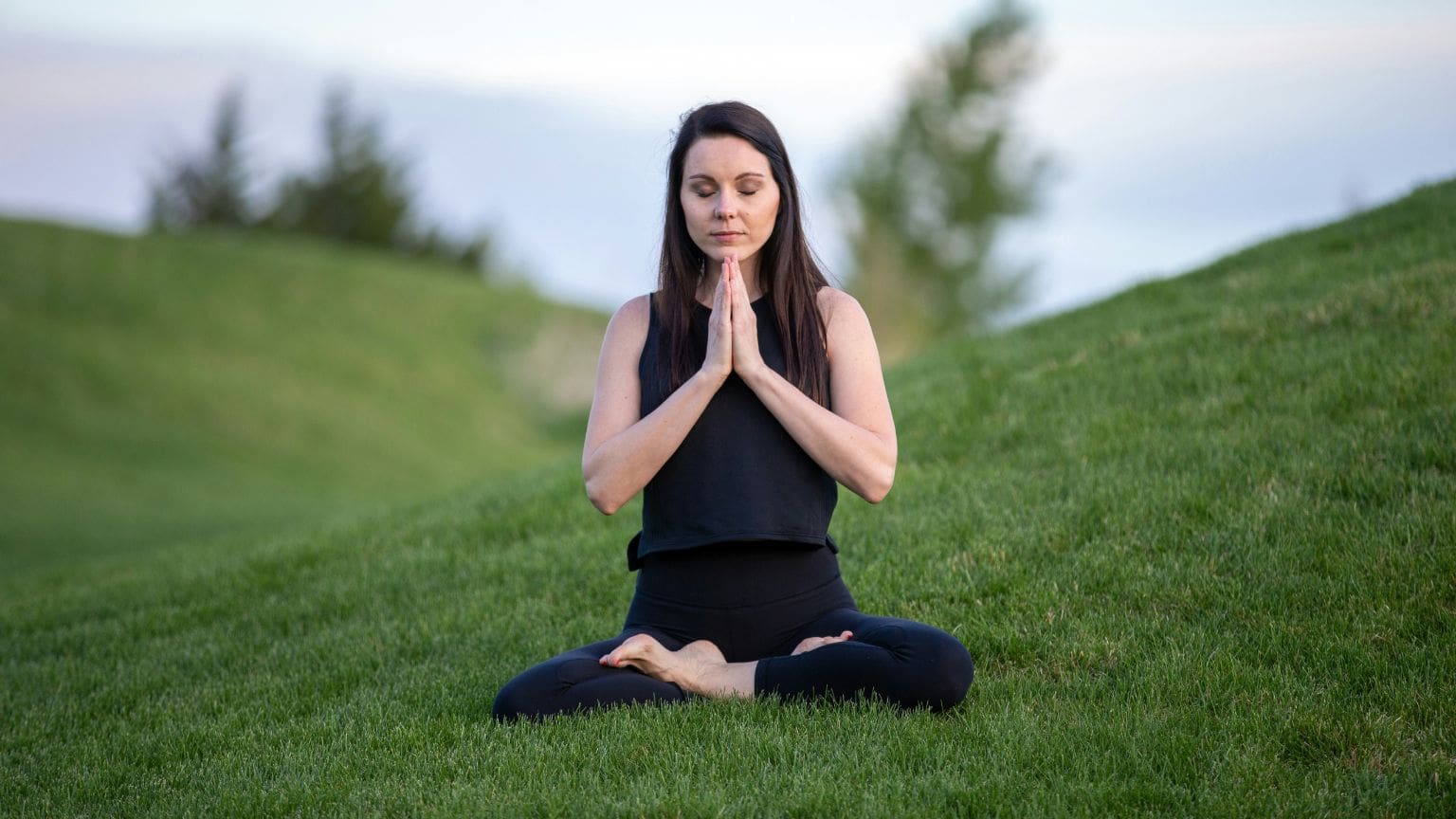 Mujer sentada en posición de loto haciendo prácticas de Meditación y respiración consciente al aire libre en España