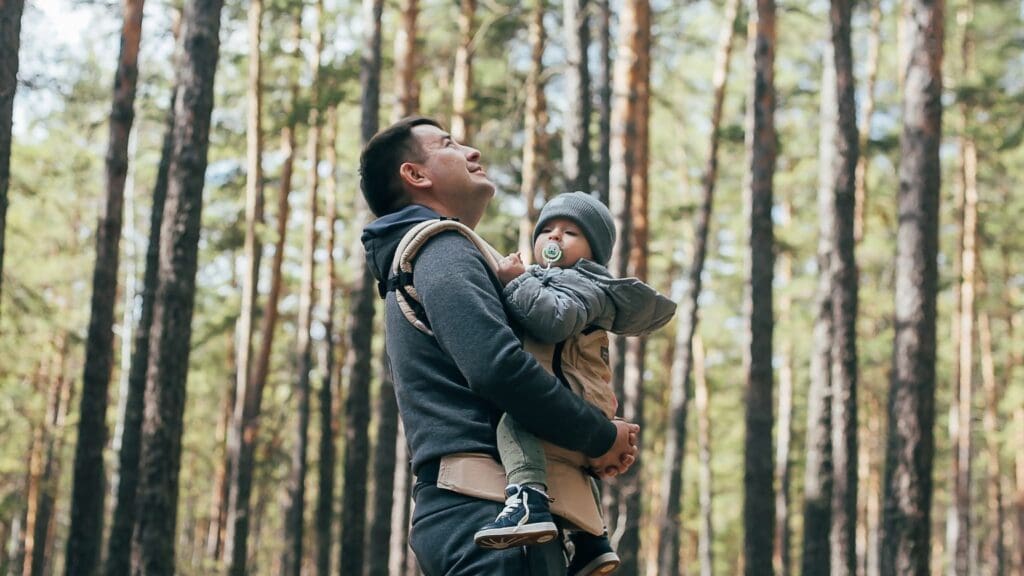 Padre y madre portando a su bebé en un portabebé ergonómico, destacando la cercanía y comodidad que proporciona el porteo seguro para el desarrollo del bebé.