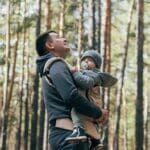 Padre y madre portando a su bebé en un portabebé ergonómico, destacando la cercanía y comodidad que proporciona el porteo seguro para el desarrollo del bebé.