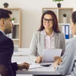 Corredor de seguros explicando las diferentes pólizas a un cliente en una reunión personalizada.