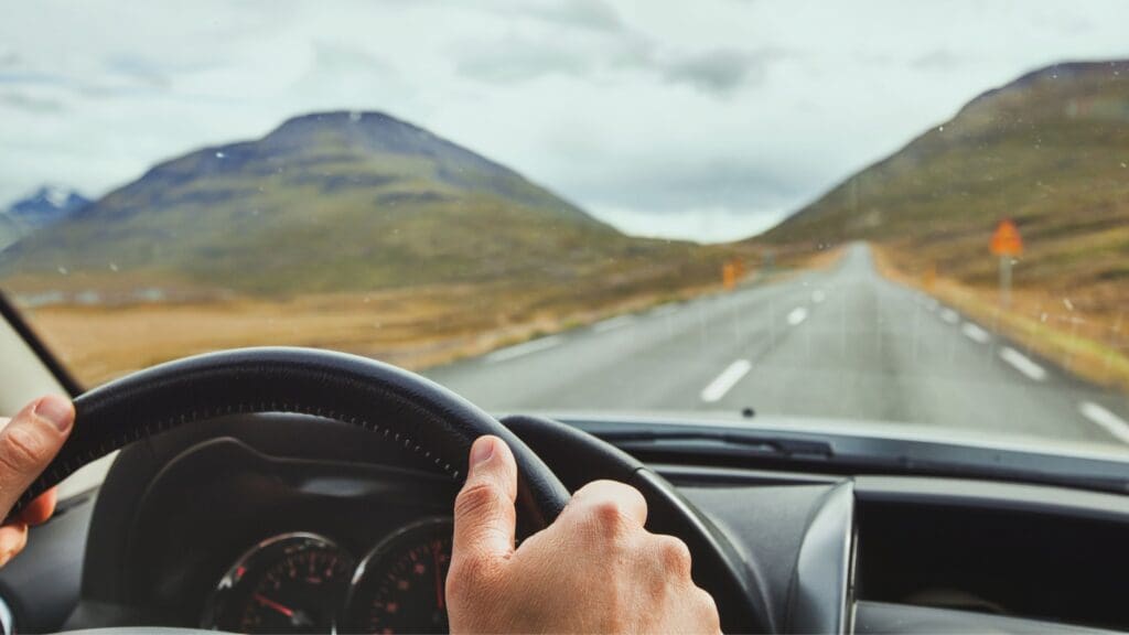 Coche deportivo de lujo recorriendo una carretera escénica en Tenerife, con vistas al océano y paisajes montañosos al fondo.