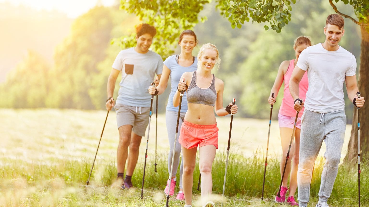 Personas practicando marcha nórdica en un sendero natural, utilizando bastones, disfrutando de la naturaleza y mejorando su salud física y mental.