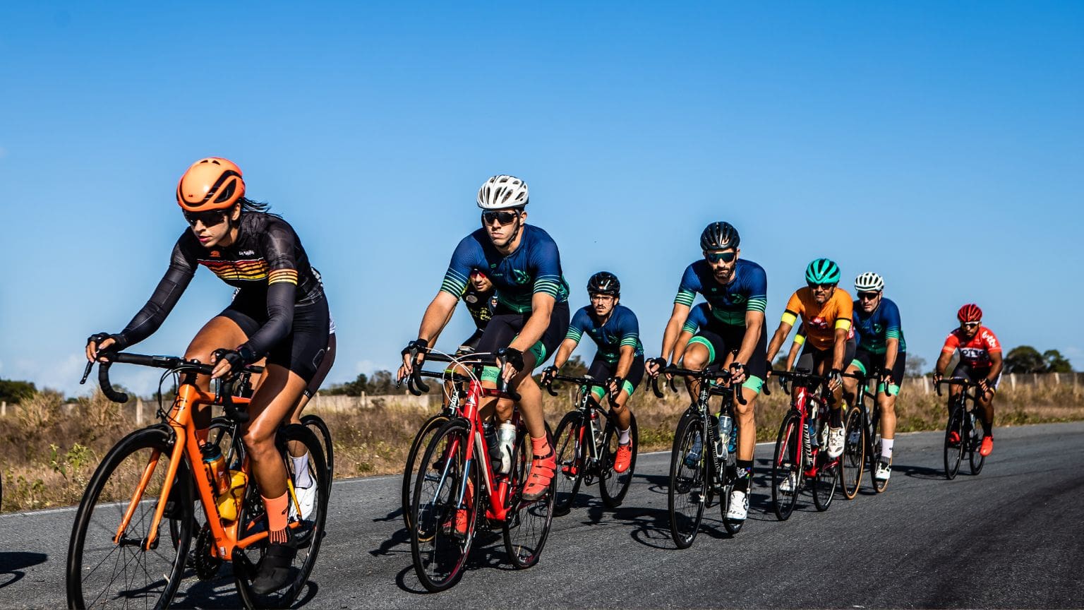 Grupo de ciclistas entrenando en una ruta al aire libre, acompañados por un entrenador profesional. Entrenamiento grupal adaptado a todos los niveles.