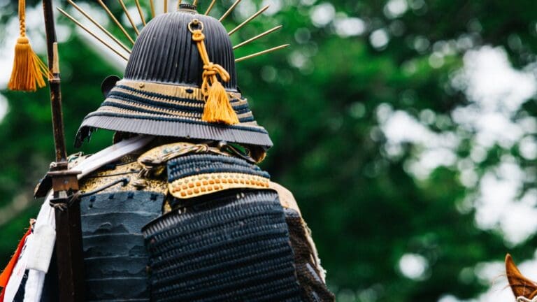 Guerrero samurái vistiendo armadura tradicional con casco decorado y adornos dorados. Esta imagen captura la esencia del legado cultural y la historia de los guerreros samuráis en Japón, un símbolo de disciplina, honor y tradición.