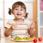 Niño disfrutando de una comida saludable con frutas y verduras para fomentar una buena nutrición.