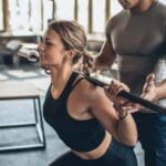 Entrenador deportivo dando consejos personalizados a un cliente en un gimnasio, ilustrando la importancia de elegir un instructor adecuado para mejorar el rendimiento físico.