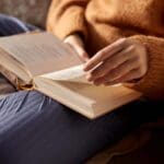 Persona leyendo un libro en un ambiente acogedor, rodeada de material de papelería y tomando notas. Representa los beneficios de la lectura y la organización personal.