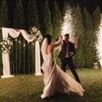 Pareja de novios sonrientes posando al aire libre durante su boda, iluminados por luz natural y rodeados de un ambiente romántico.