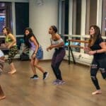 Grupo de personas practicando baile en un estudio profesional con espejos, demostrando técnica y pasión por la danza.