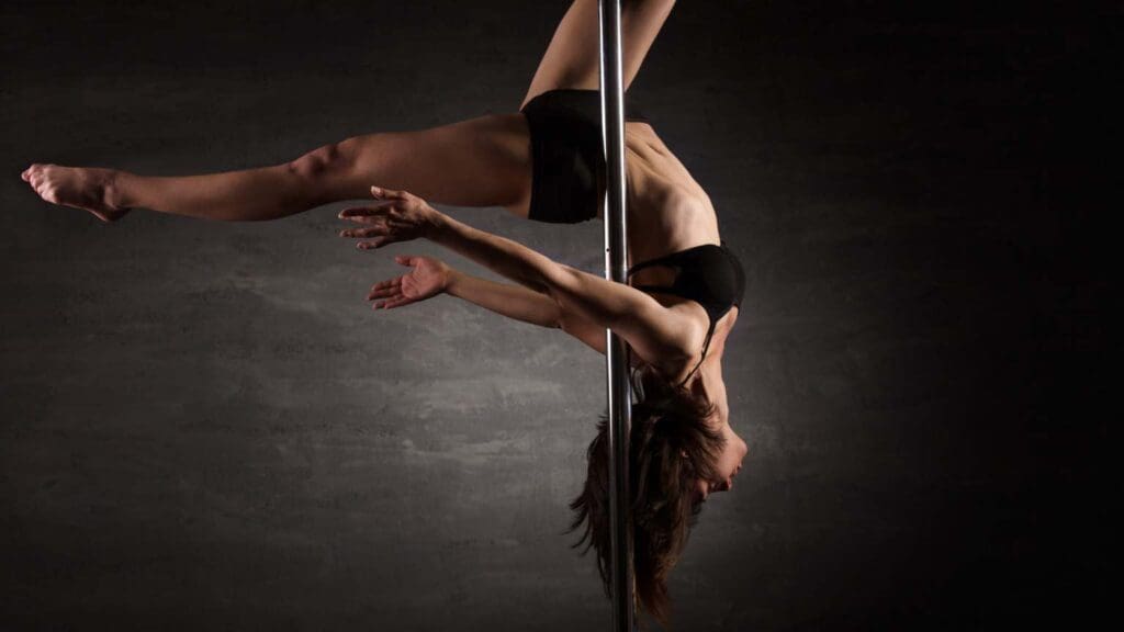 Mujer practicando pole dance en un estudio, demostrando fuerza, flexibilidad y elegancia en una barra vertical. Actividad que combina ejercicio físico y expresión artística.