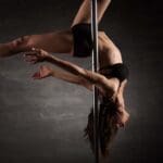 Mujer practicando pole dance en un estudio, demostrando fuerza, flexibilidad y elegancia en una barra vertical. Actividad que combina ejercicio físico y expresión artística.