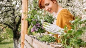 Persona cuidando un huerto urbano ecológico en una terraza, con macetas y mesas de cultivo llenas de plantas frescas.