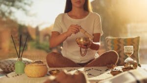 Mujer practicando meditación con un cuenco tibetano, rodeada de elementos de relajación en un ambiente cálido y natural.