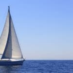 Velero navegando frente a una cala con aguas cristalinas en Mallorca, ideal para explorar playas y calas inaccesibles por tierra.