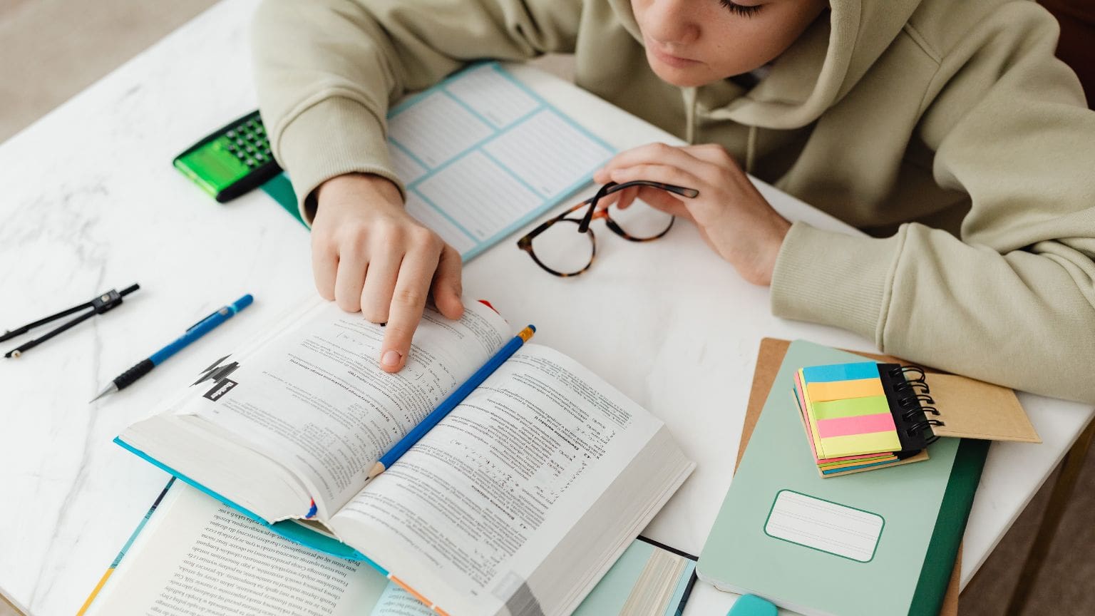 Estudiante concentrado utilizando técnicas de estudio efectivas con libros y portátil en un espacio organizado y acogedor, representando aprendizaje productivo.