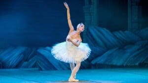 Bailarines en escena realizando una coreografía artística que combina ballet clásico y danza contemporánea en un teatro iluminado.