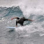 Surfista principiante disfrutando de una clase de surf en las playas soleadas de Fuerteventura, rodeado de olas suaves y paisajes espectaculares.