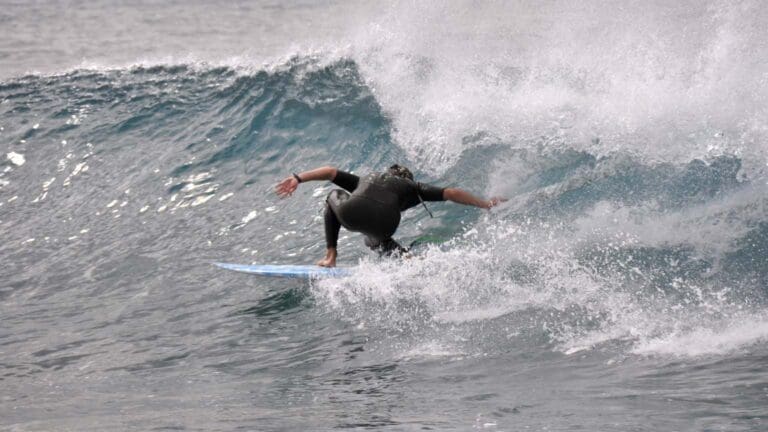 Surfista principiante disfrutando de una clase de surf en las playas soleadas de Fuerteventura, rodeado de olas suaves y paisajes espectaculares.