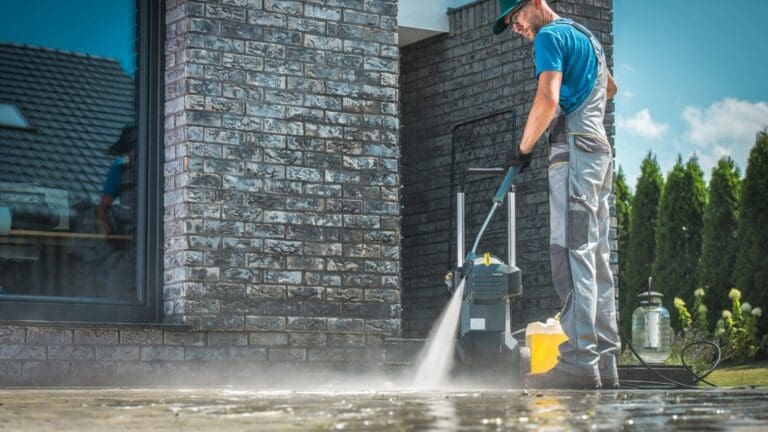 Trabajador limpiando una fachada con una hidrolimpiadora de agua a presión. Espacio exterior impecable después de un servicio profesional.