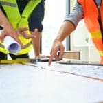 Equipo de arquitectos e ingenieros revisando planos en una obra en construcción, representando la gestión eficiente de proyectos arquitectónicos y reformas.