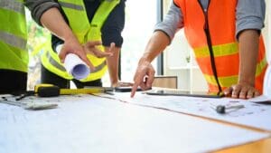 Equipo de arquitectos e ingenieros revisando planos en una obra en construcción, representando la gestión eficiente de proyectos arquitectónicos y reformas.