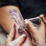 Professional tattoo artist creating a detailed forearm tattoo in a clean studio