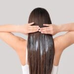 Mujer con cabello sano y brillante aplicando un tratamiento capilar natural para regeneración y fortalecimiento.