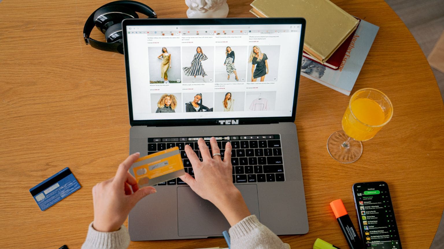 Mujer feliz comprando ropa de mujer online desde su portátil, rodeada de prendas modernas y elegantes