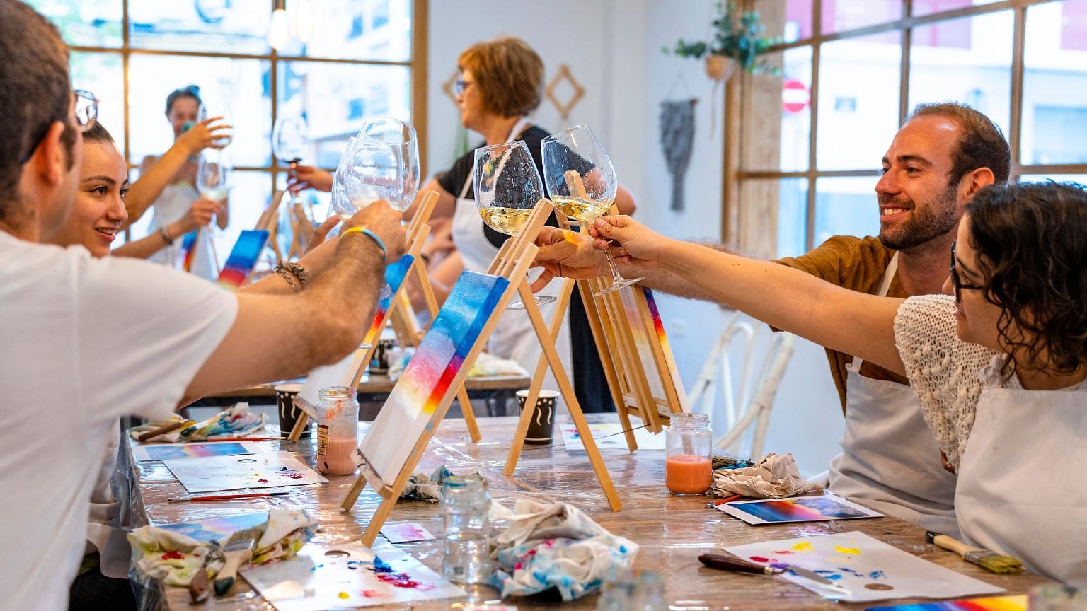 Personas disfrutando de un taller de pintura y vino, creando arte en un ambiente acogedor y relajado.