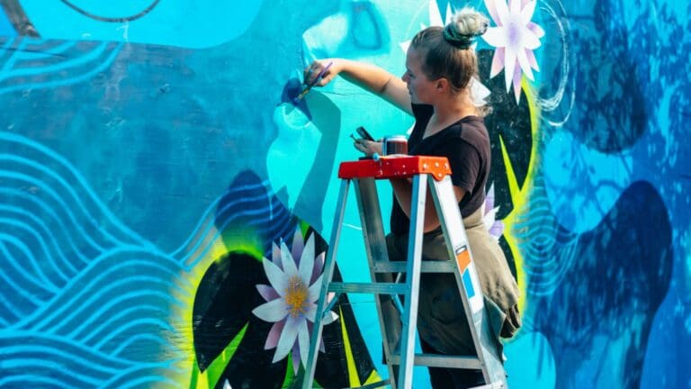 Artista pintando un mural decorativo en una pared, aplicando técnicas de pintura mural para transformar el espacio con arte y color.