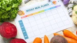 Mesa con alimentos saludables, frutas frescas y un planificador semanal de comidas, representando un estilo de vida con alimentación equilibrada.