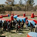 Jugadores principiantes equipados recibiendo instrucciones en un campo de paintball al aire libre