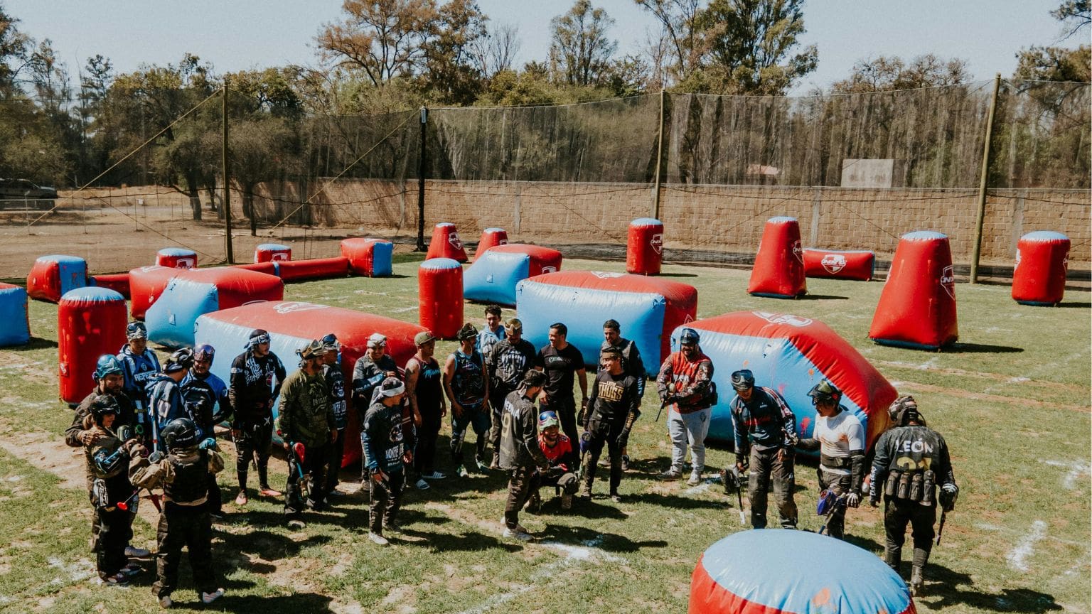 Jugadores principiantes equipados recibiendo instrucciones en un campo de paintball al aire libre
