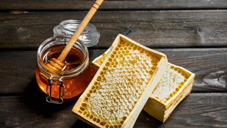 Frasco de miel pura artesanal con panal natural y cuchara de madera sobre fondo rústico de madera.