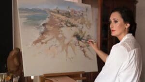 Mujer artista pintando un cuadro al óleo en su estudio con luz natural y estilo figurativo impresionista.