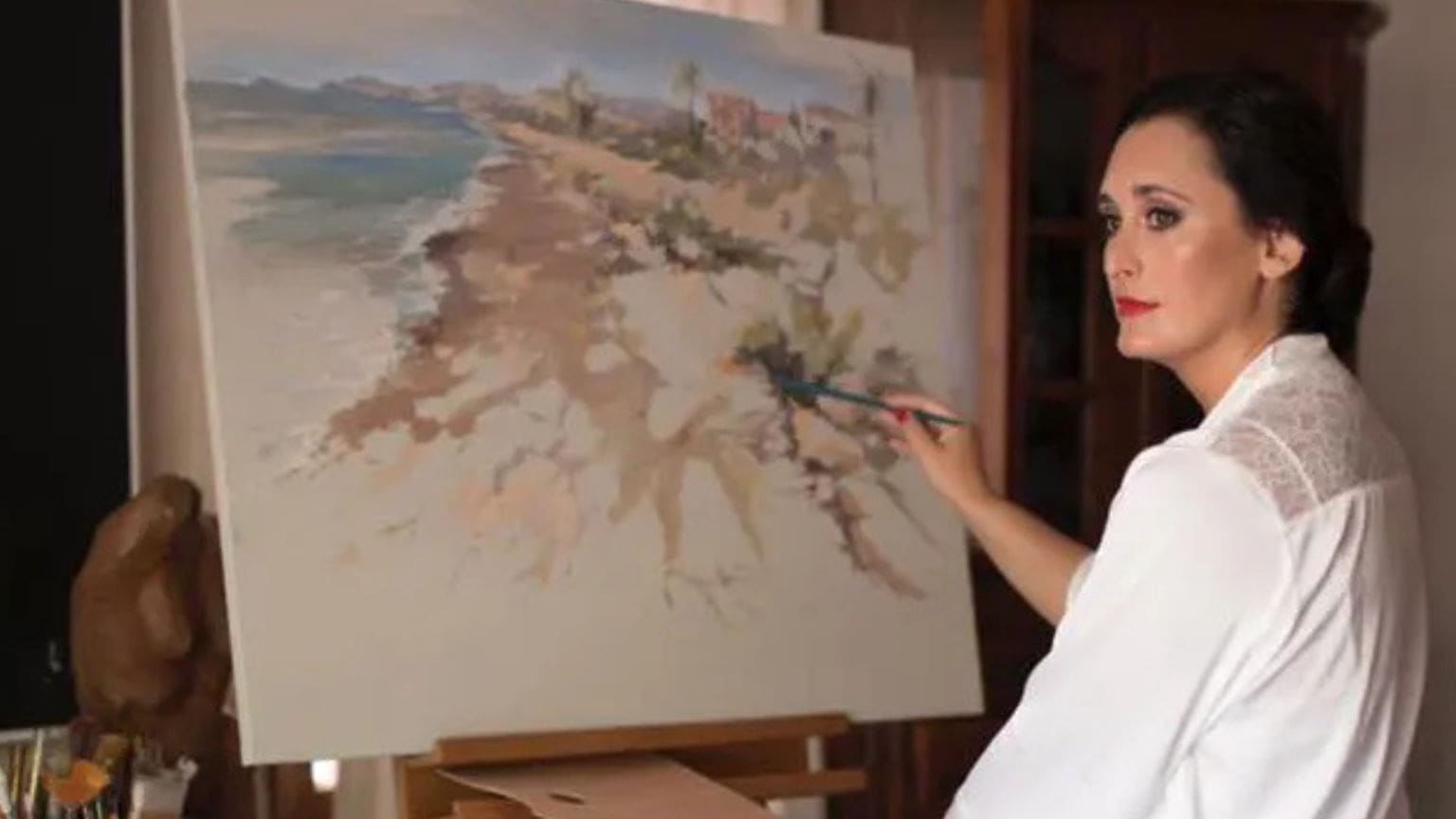 Mujer artista pintando un cuadro al óleo en su estudio con luz natural y estilo figurativo impresionista.