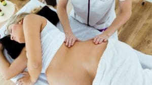 Mujer embarazada recibiendo masaje prenatal profesional en camilla, con apoyo lateral para favorecer su bienestar y relajación.