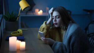 Mujer en casa durante un apagón, usando el móvil con expresión preocupada, iluminada por velas, representando el impacto del corte eléctrico en el hogar.