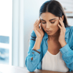 Mujer con expresión de dolor tocándose la sien, posible síntoma de migraña causada por tensión mandibular.