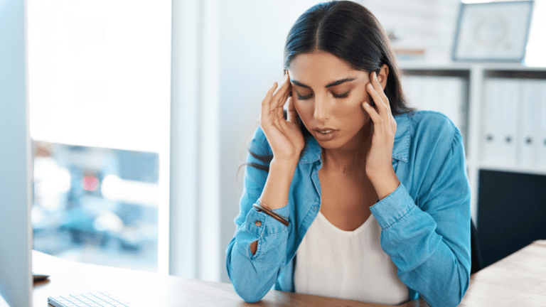Mujer con expresión de dolor tocándose la sien, posible síntoma de migraña causada por tensión mandibular.