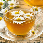 Taza de infusión de manzanilla caliente sobre mesa de madera con flores secas alrededor, ideal para el bienestar digestivo y la salud intestinal.