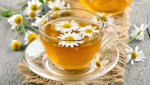 Taza de infusión de manzanilla caliente sobre mesa de madera con flores secas alrededor, ideal para el bienestar digestivo y la salud intestinal.