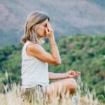 Mujer practicando breathwork al aire libre en entorno natural durante un retiro espiritual, simbolizando conexión, respiración consciente y bienestar holístico.