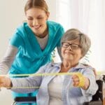 Profesional en rehabilitación neurológica ayudando a adulto mayor en proceso de recuperación tras ictus en entorno terapéutico adaptado.