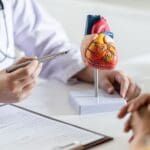 Consulta médica para la prevención de enfermedades cardíacas, con corazón rojo y estetoscopio sobre mesa blanca, simbolizando la salud cardiovascular.